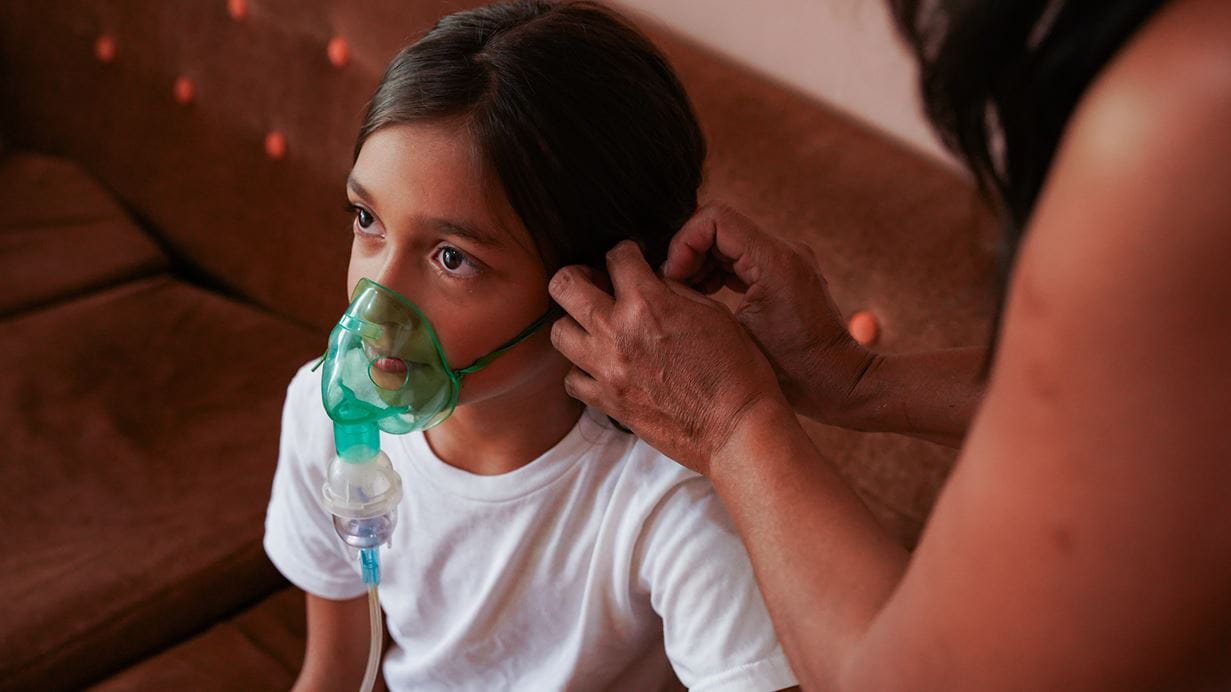Valery sits still while her grandmother helps her use the nebuliser which assists her breathing.