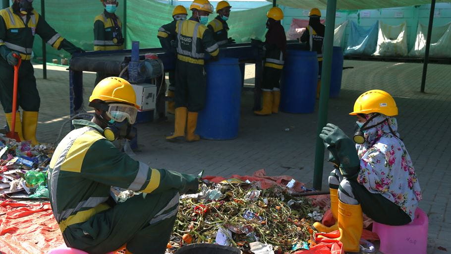 Men and women wearing personal protective equipment work sorting waste at the Haryali Hub in Pakistan.