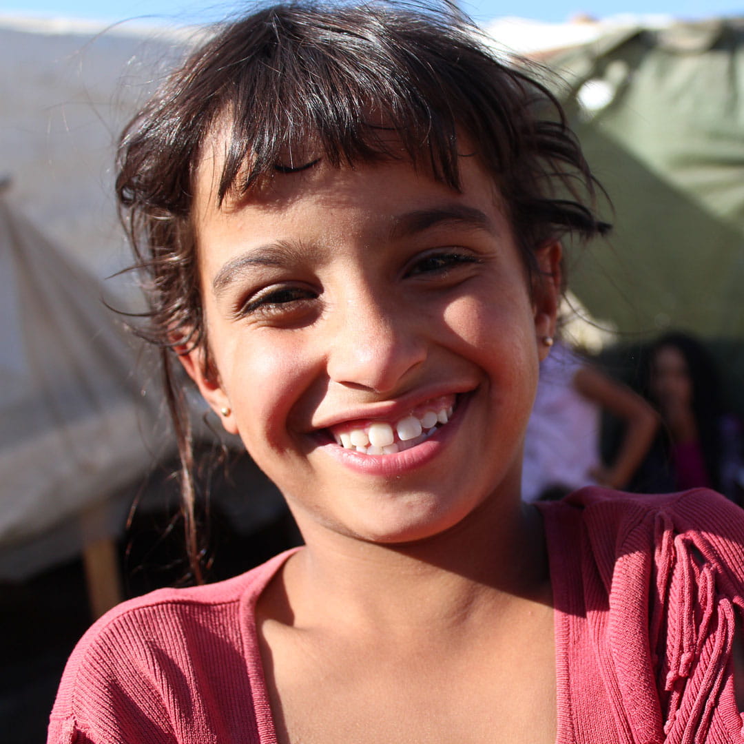 Yasmin, aged 9, smiles while standing in a refugee camp.