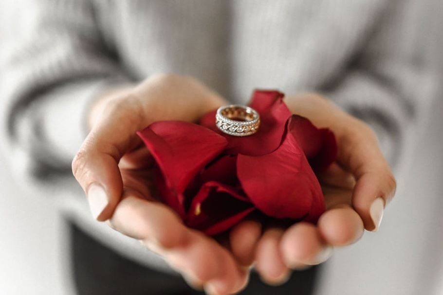 Person holds silver ring on cushion of roses.