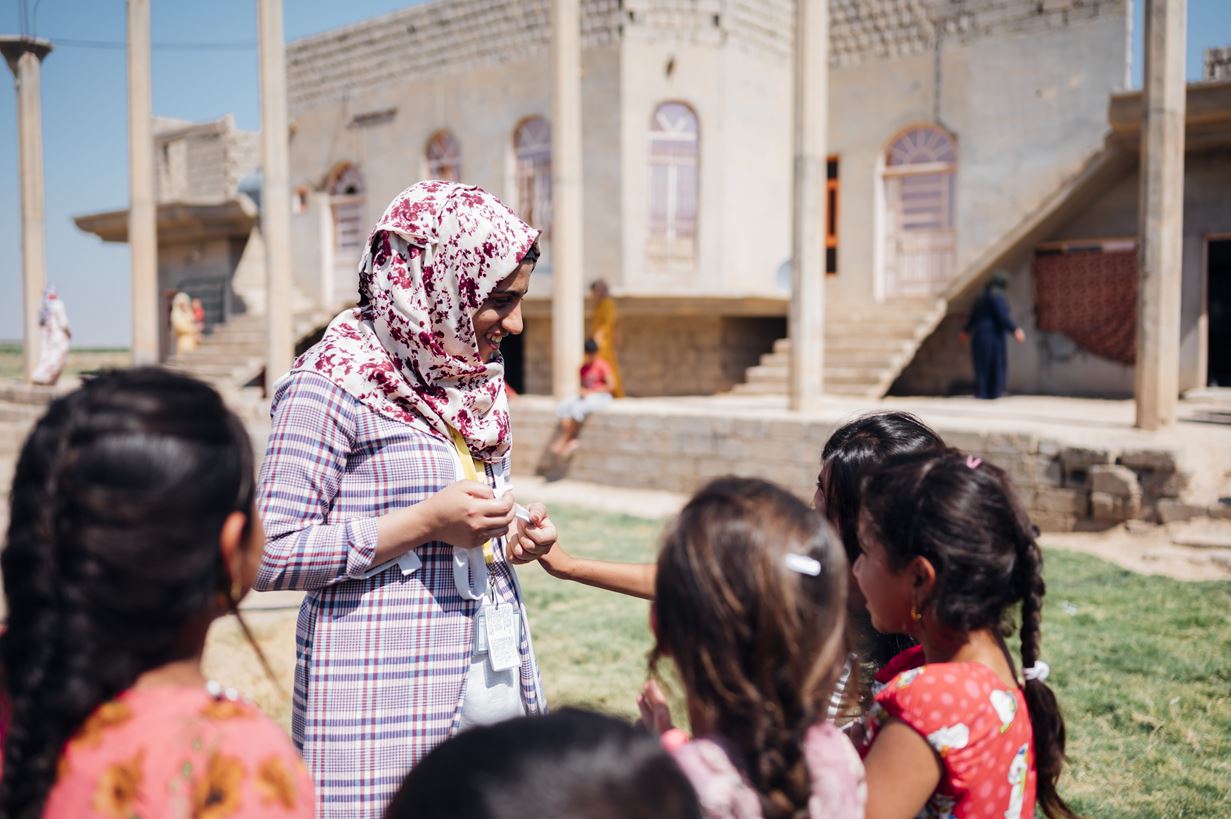 A woman is stood smiling and talking to a small group of girls