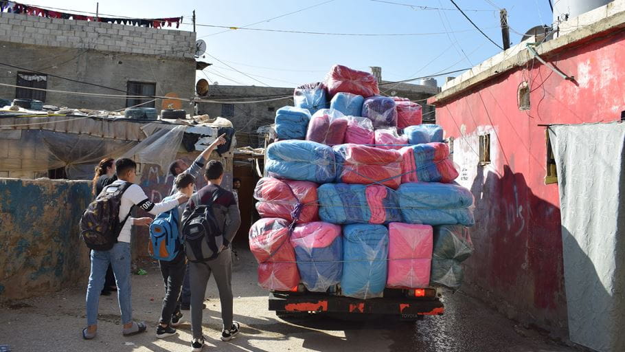 A group of people walk by and look at a truck piled with plastic wrapped blankets.
