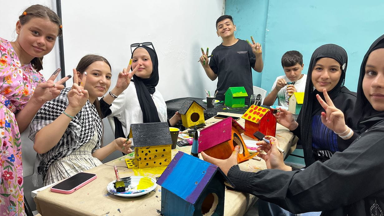 A group of children sit around a table painting bird houses.