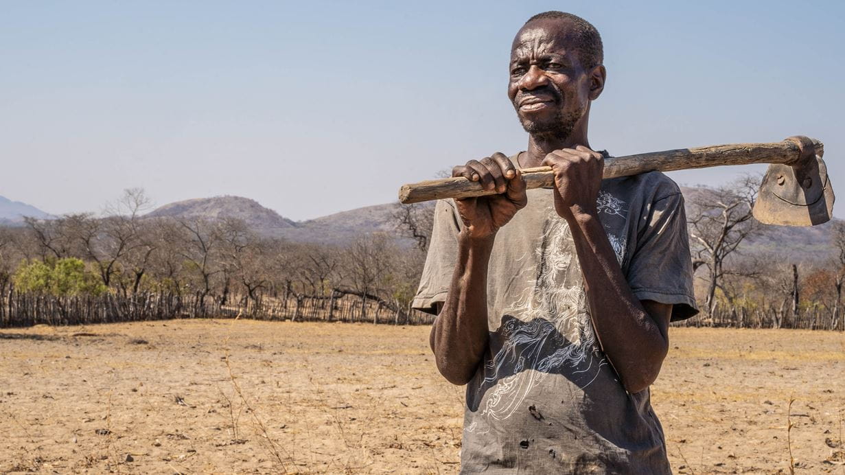 Person standing in a barren farm holding a farming tool