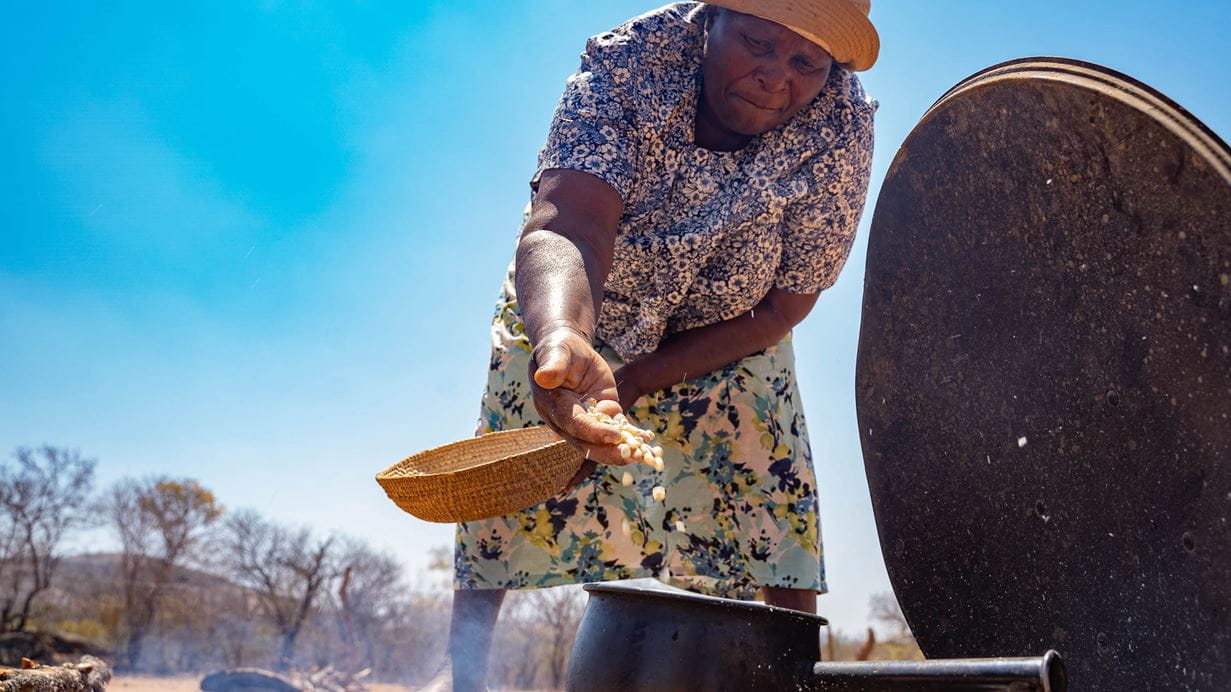 Person pours a handful of maize into a boiling pot