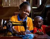 A woman uses a sewing machine with a child sat next to her.