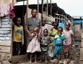 A family stand together in front of house made from wood and metal sheets.
