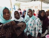 Group of women in hijabs sitting and looking intently, some in turquoise, in a gathering.