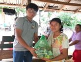 A man and woman hold up a plastic bag up to the camera, filled with food.