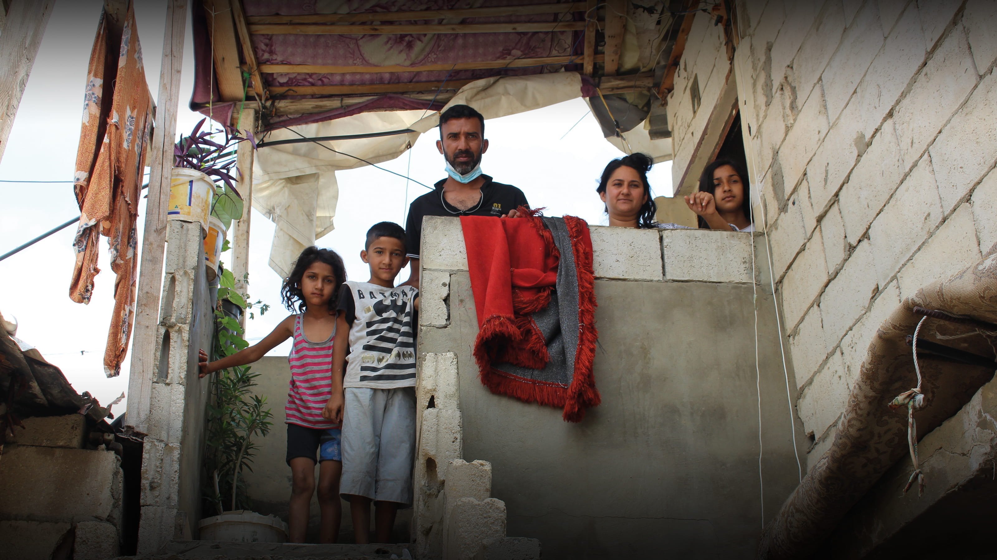 Family pictured outside unsafe housing. Tearfund’s church partners are helping by offering practical support and showing compassion.