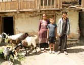 Three people standing outside a building, next to them are several goats.
