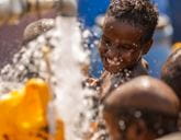 A boy smiles as water pours from a tap into a container.