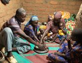 A family sat on the floor around a metal plate. The parents and two of the children reach to get food from the plate.