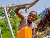 A child turns a tap as water fills a yellow water container.