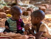 Two small children sitting together on the ground