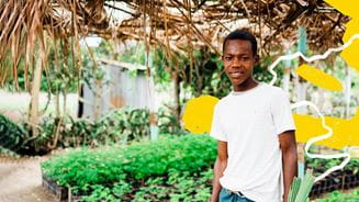 A person standing outside in front of a community garden looks at the camera and smiles