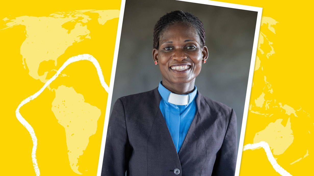 A woman wearing a jacket with a blue shirt and a clerical collar smiles broadly.