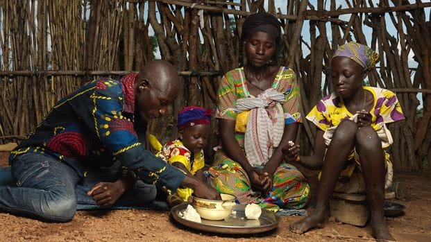 A man, woman and two children sitting on the floor sharing a meal.