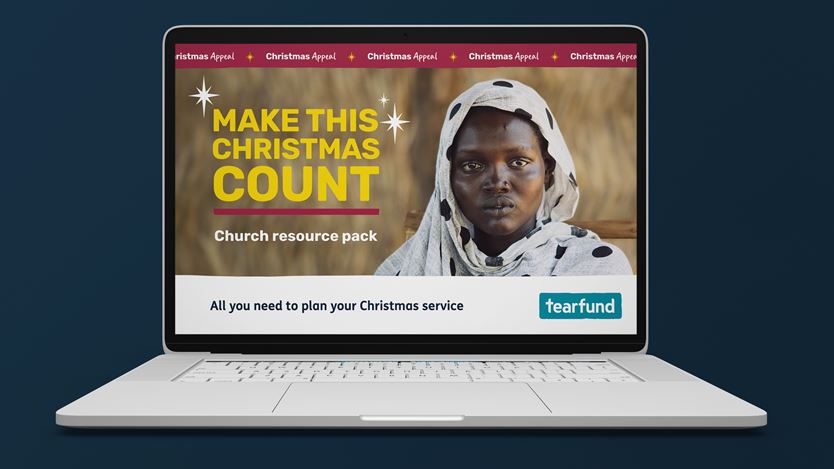 A silver laptop angled on a dark blue background, displaying a webpage for a 'Christmas Appeal'. The page features the text 'MAKE THIS CHRISTMAS COUNT' alongside a woman wearing a light, spotted headscarf. Below, it reads 'Church resource pack' and 'All you need to plan your Christmas service' with the Tearfund logo.