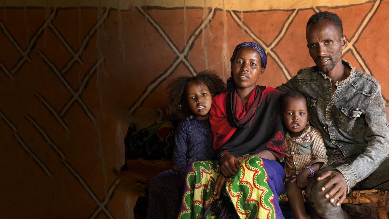 A man and woman are sat, holding their children beside them.