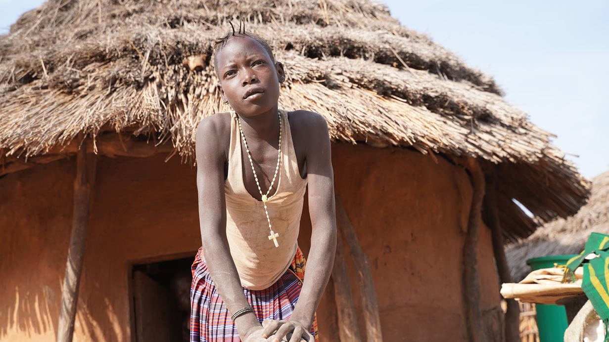 12-year-old Lucie from Uganda stands outside her home as she helps prepare a meal for her family.