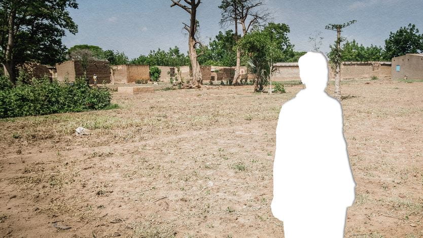 A photograph of several buildings in the distance and a dry field in the foreground with a silhouette cut out of a person in white. 