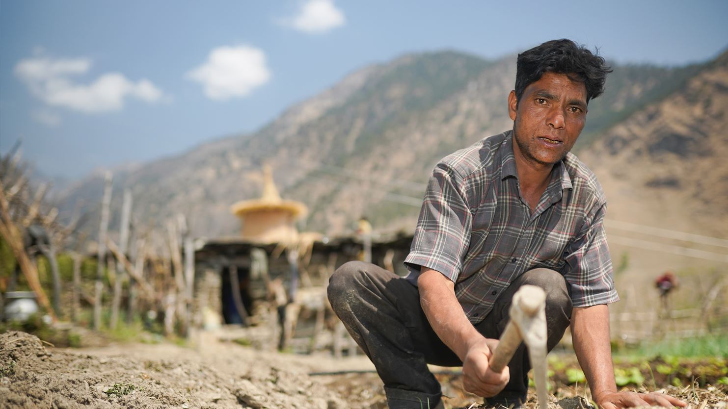 A man using a farming tool with mountains in the background