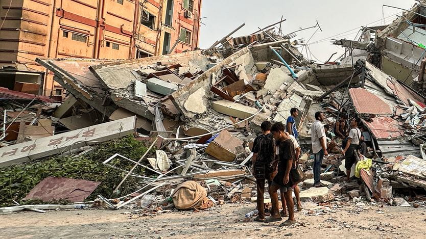 Several people are stood in front of the debris of a collapsed building in Mandalay, Myanmar. 