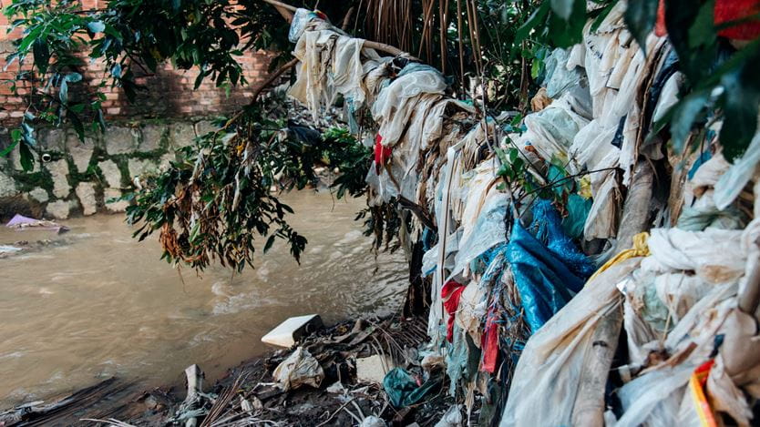 Plastic waste hangs from tree branches and clogs up water in the river.
