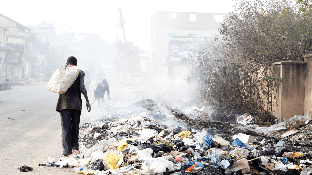 A man and woman walking on a road next to piles of dumped, burning waste.