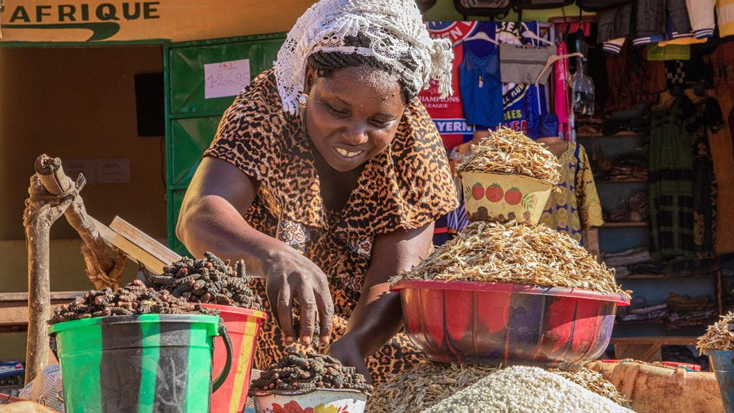 A woman smiles and leans over a bowl of produce, around her are more buckets and bowls.
