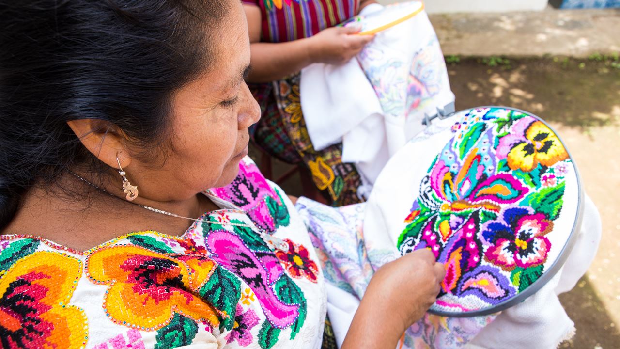 A woman embroidering a detailed colourful flower design