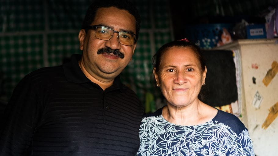 Close-up of a smiling man and woman standing side-by-side in what looks like a home.