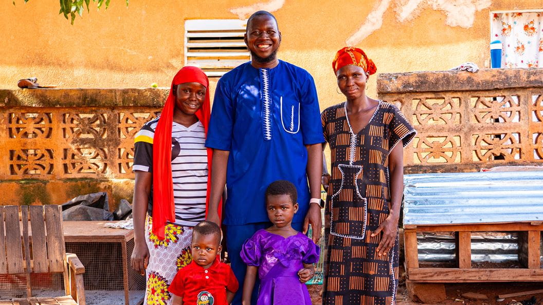 A family photo of Gauthier, his wife and two children outside their home in Mali. They are smiling together.