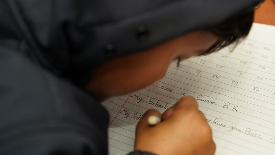 Close-up of a child's hand writing on lined paper during a lesson.