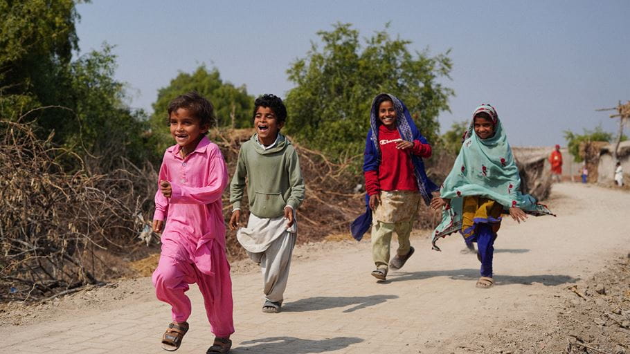 Four children run down a dusty pathway laughing and smiling.