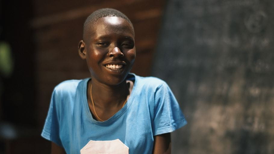 Portrait of a smiling young Black woman in a blue shirt, looking directly at the viewer.
