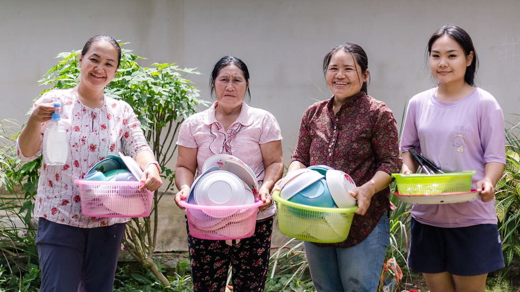 Four women holding up baskets of plates to be washed