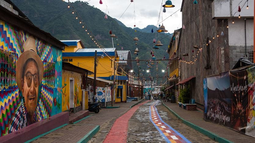A brightly painted street, lined with lamps and festoon lights strung overhead