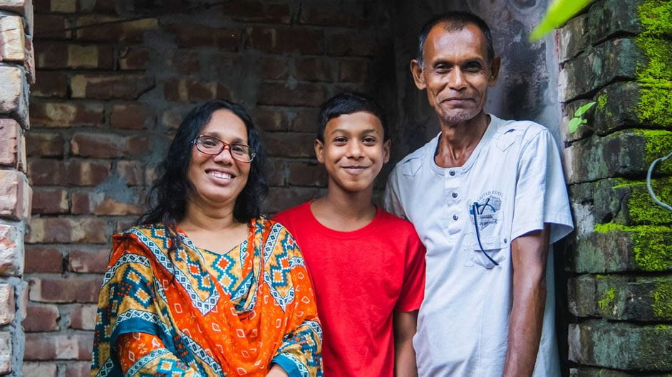 A woman a child and a man stand together smiling to the camera.
