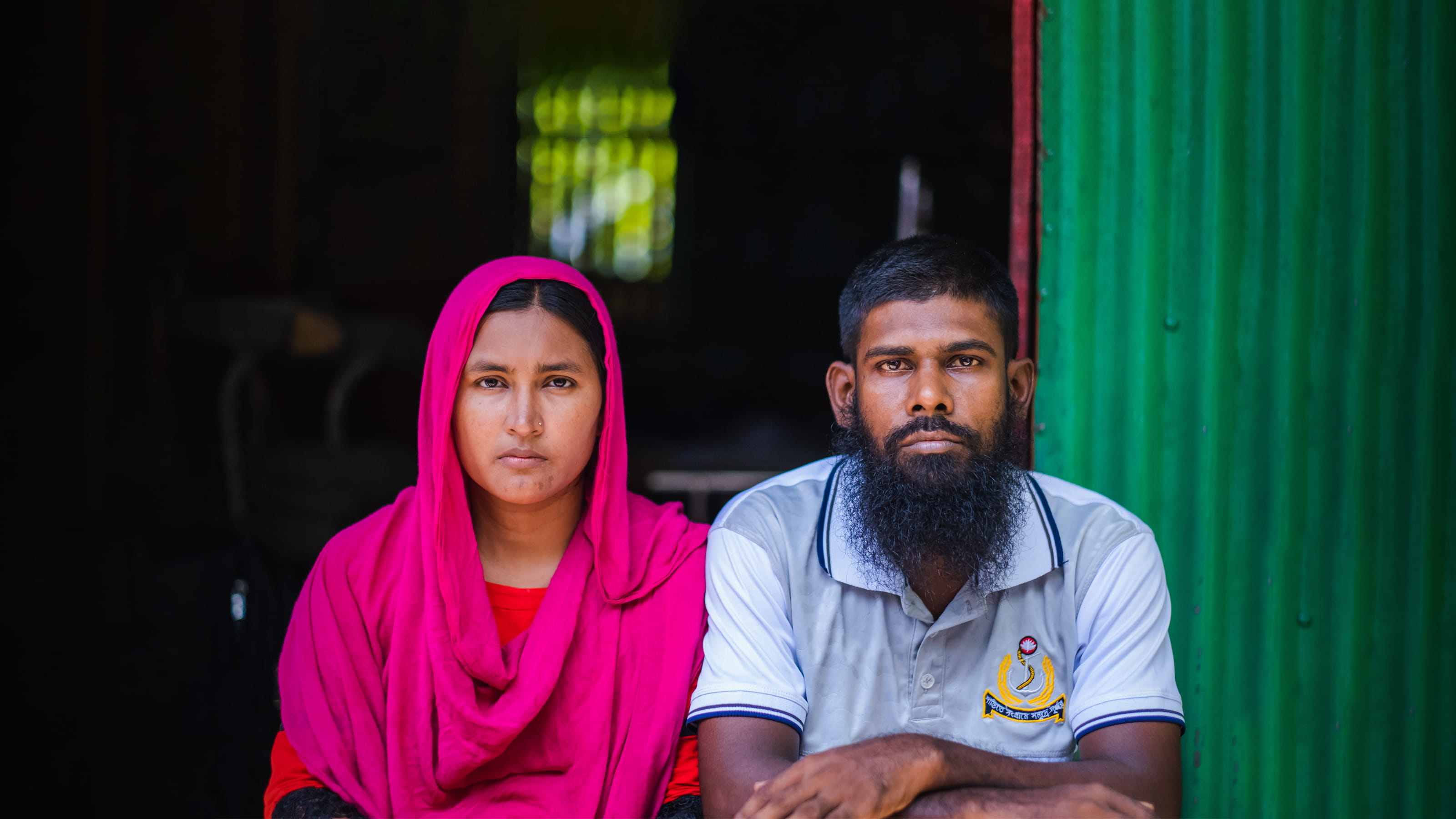 A woman and a man sit side by side looking directly at the camera.