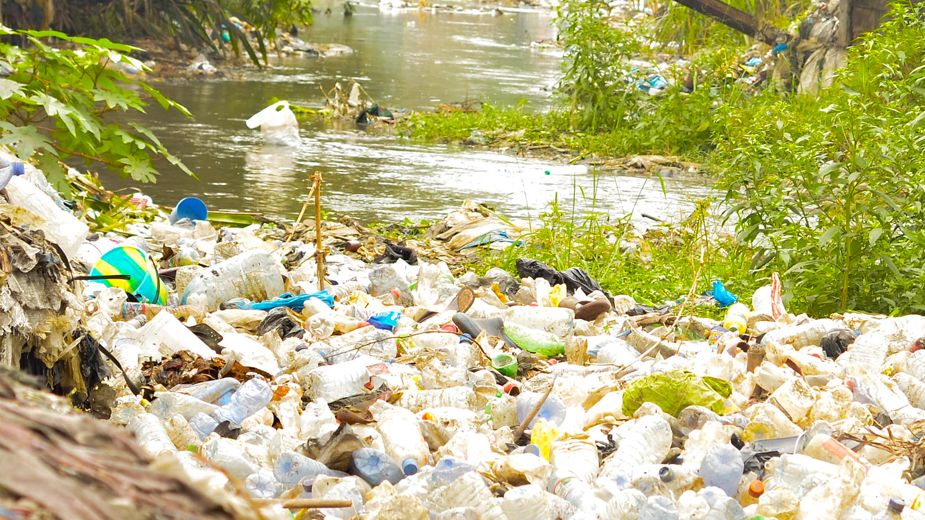 Lots of plastic waste in heaps on the edge of a river bed.