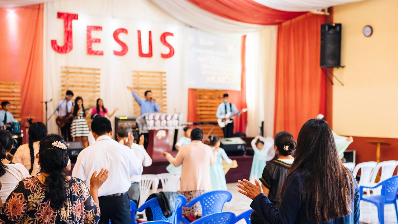 People worshiping in a church with the word Jesus in big letters on the wall