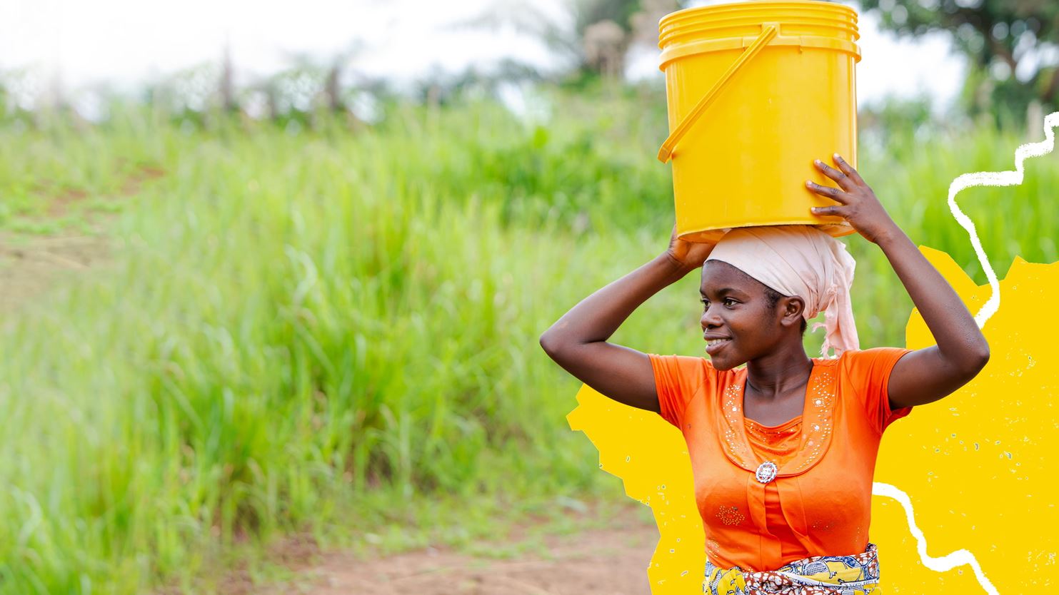 A women wearing orange is carrying a yellow bucket on her head.