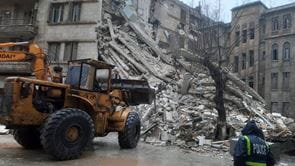 A construction backhoe loader in front of a collapsed building
