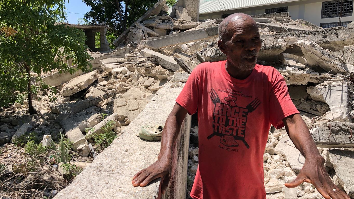 Man standing in front of building in Haiti destroyed by an earthquake