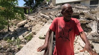Man standing in front of building in Haiti destroyed by an earthquake