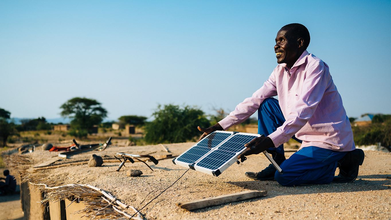 A man in Tanzania cleans, maintains and positions the solar panel on the roof of his house (Tom Price - Ecce Opus/Tearfund)