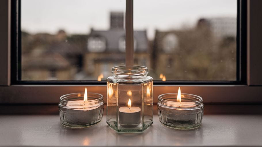 Three small candles flicker on a windowsill against a backdrop of houses.  