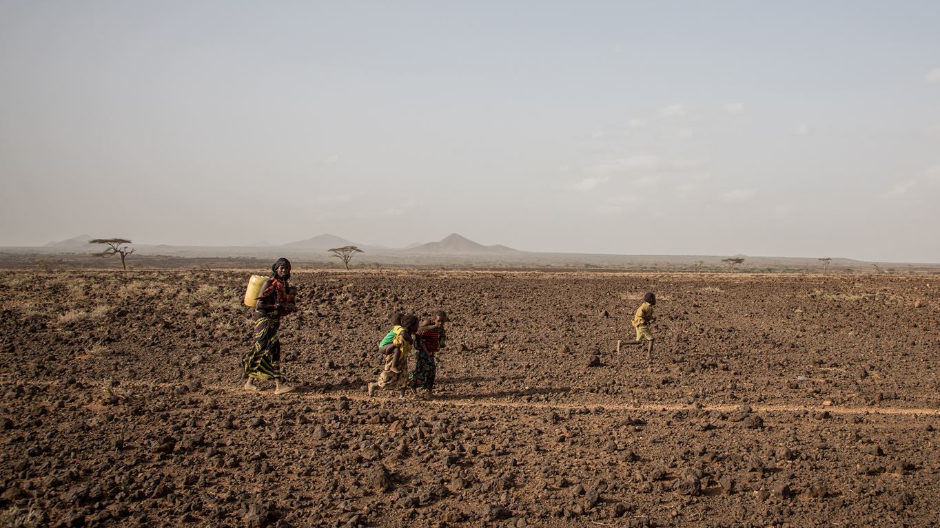 Woman and two children walking across arid, dry land